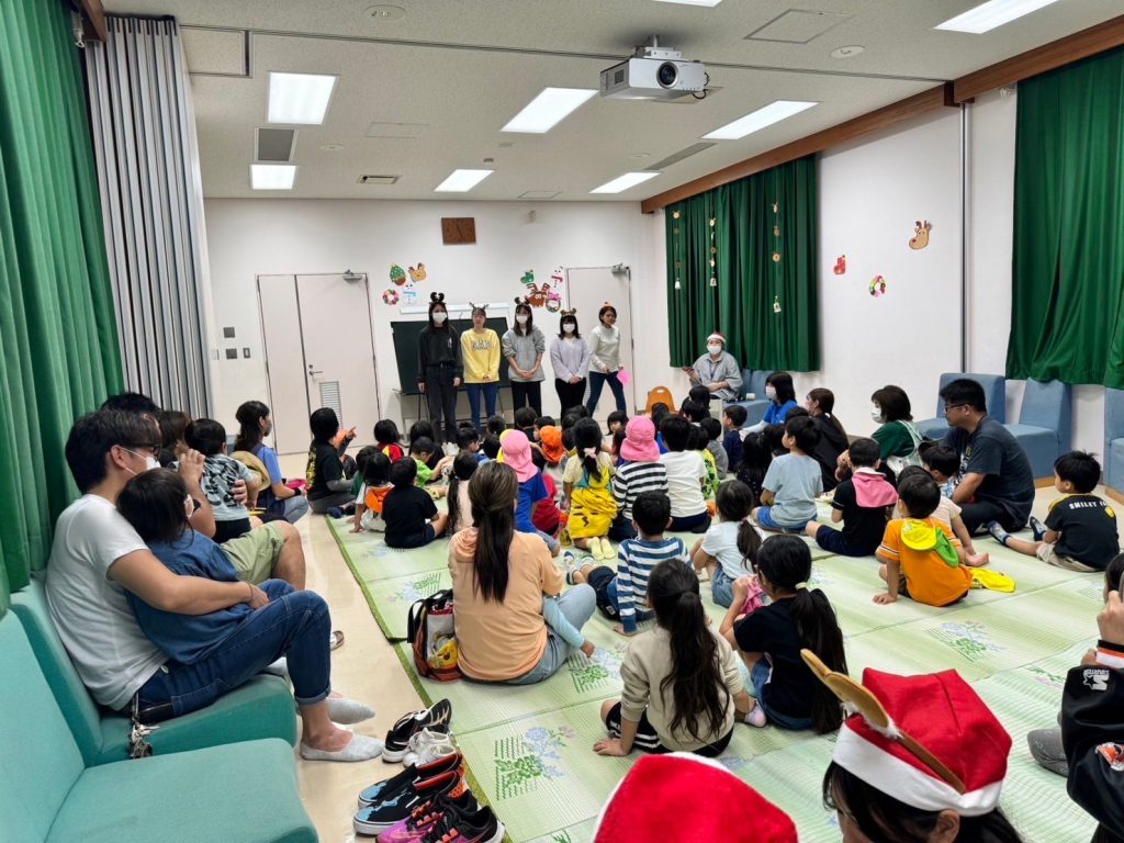 琉リハのこども保育リハビリ学科の学生が、金武町のこどもたちの前で読み聞かせをしている様子